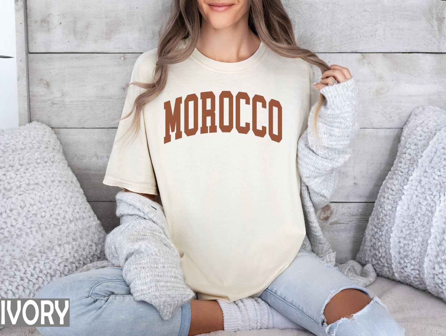 a woman sitting on a bed wearing a shirt that says morocco