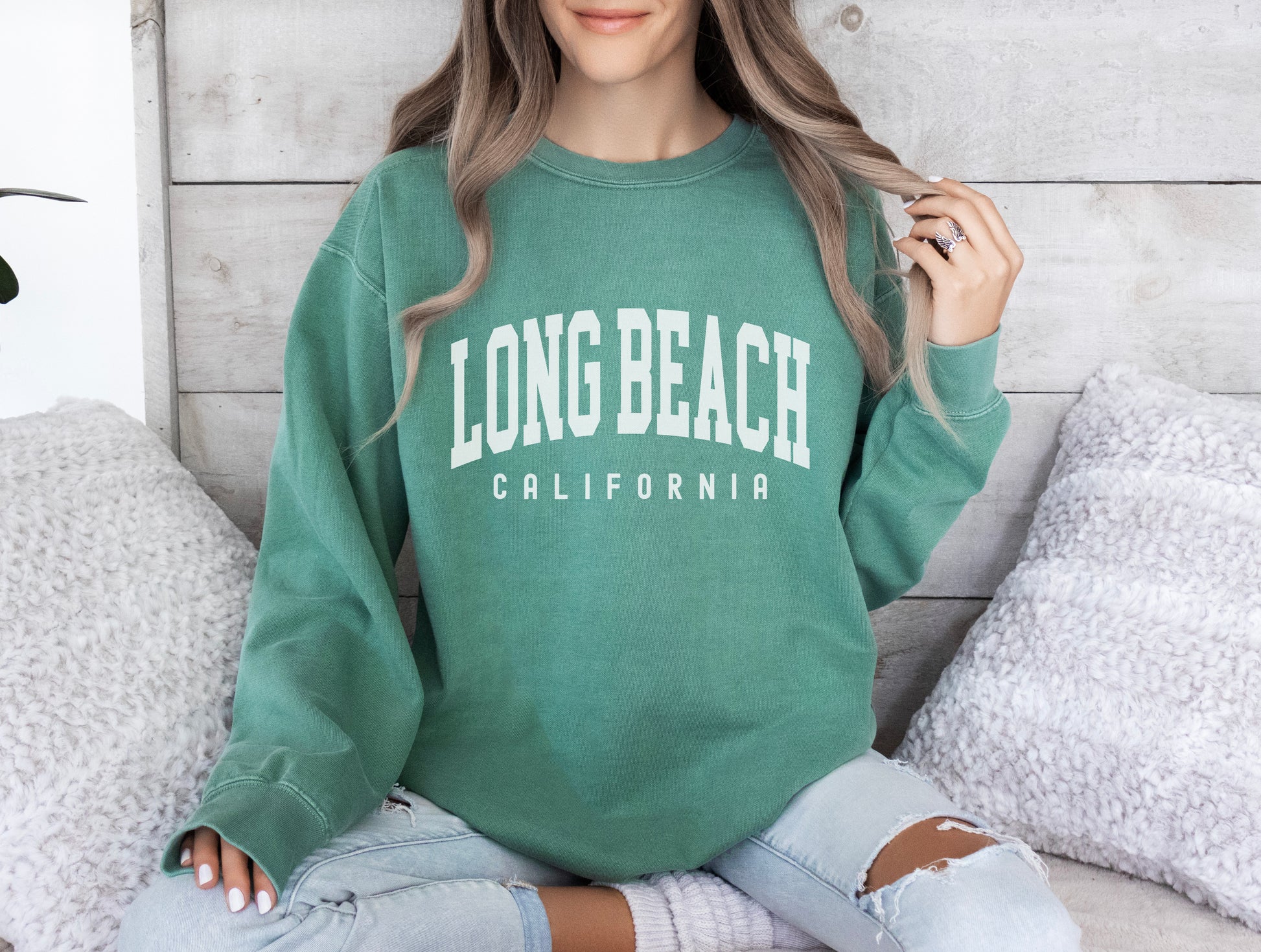 a woman sitting on a bed wearing a long beach california sweatshirt