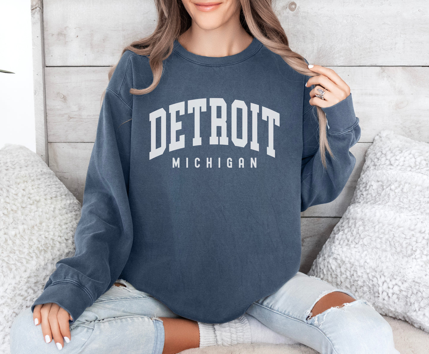 a woman sitting on a bed wearing a detroit sweatshirt