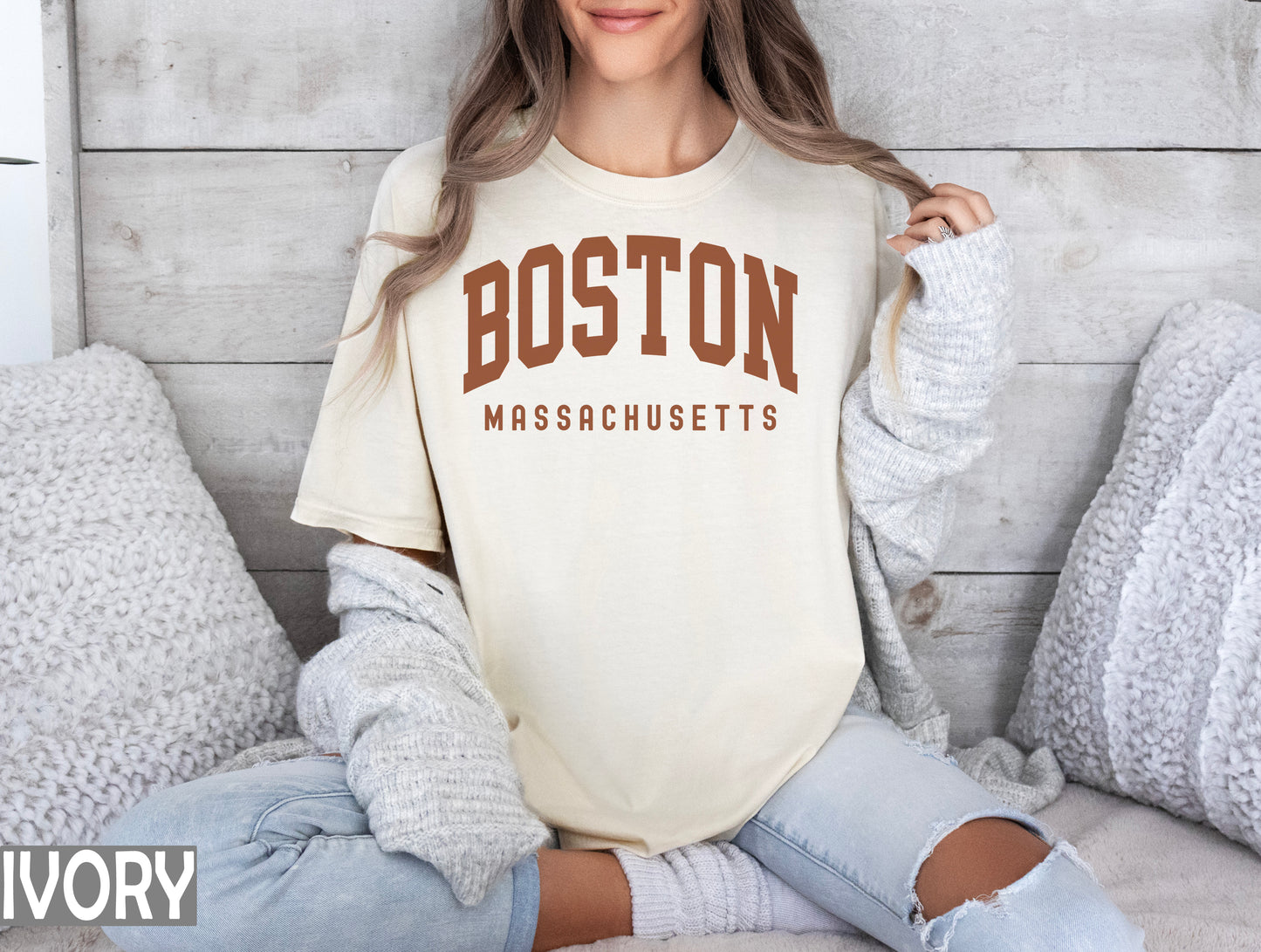 a woman sitting on a bed wearing a boston massachusetts t - shirt