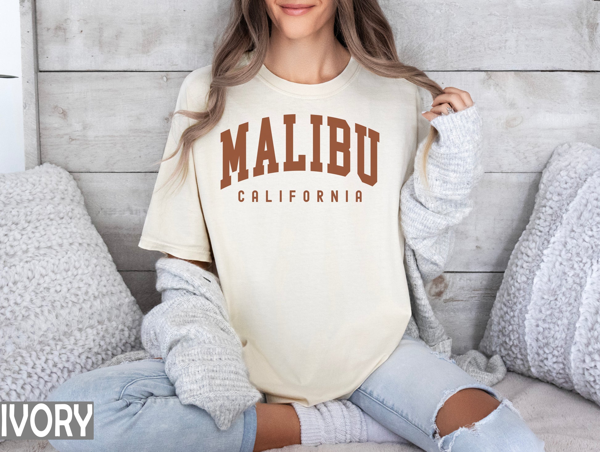 a woman sitting on a bed wearing a shirt that says malibu california