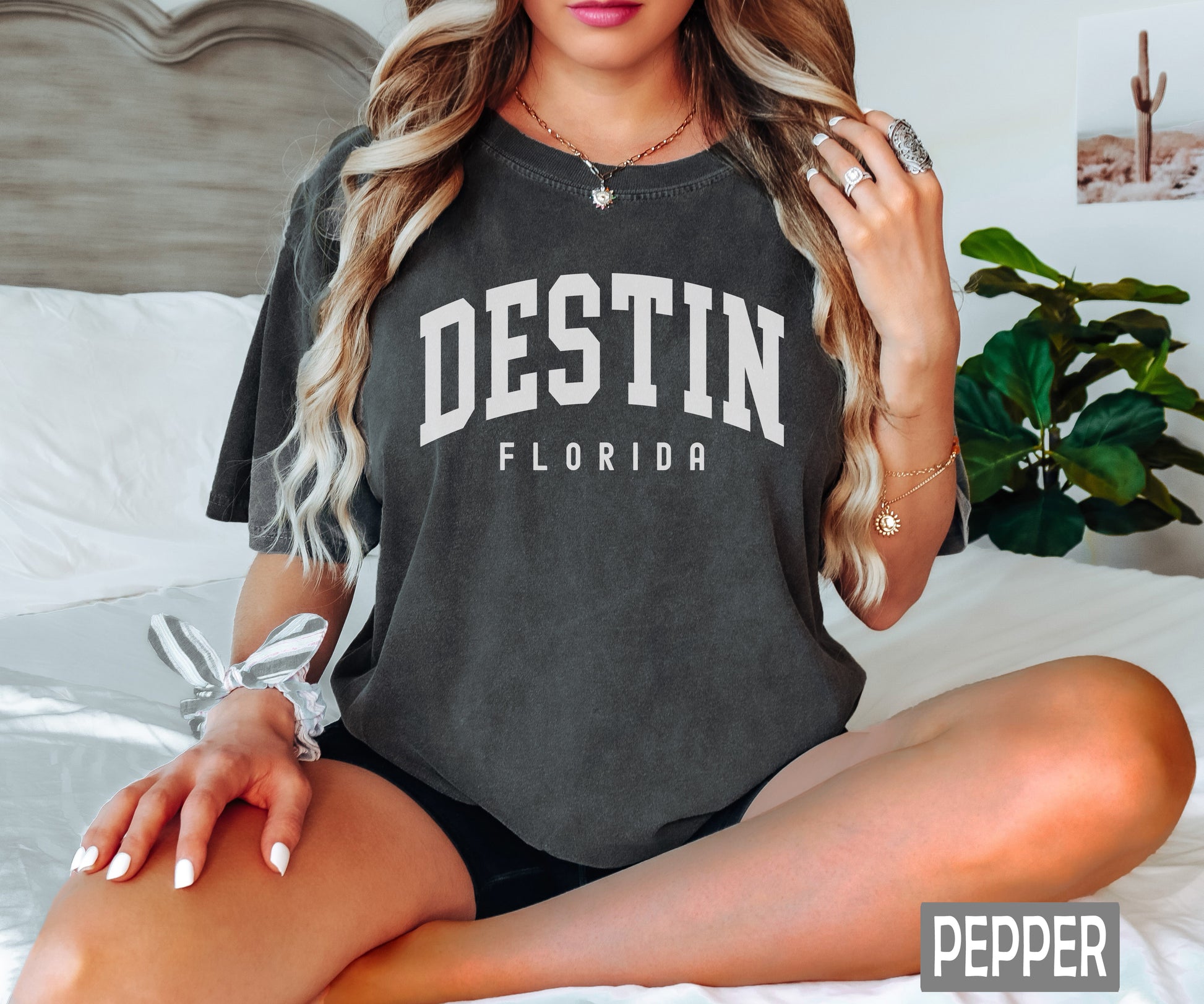 a woman sitting on a bed wearing a shirt that says destin