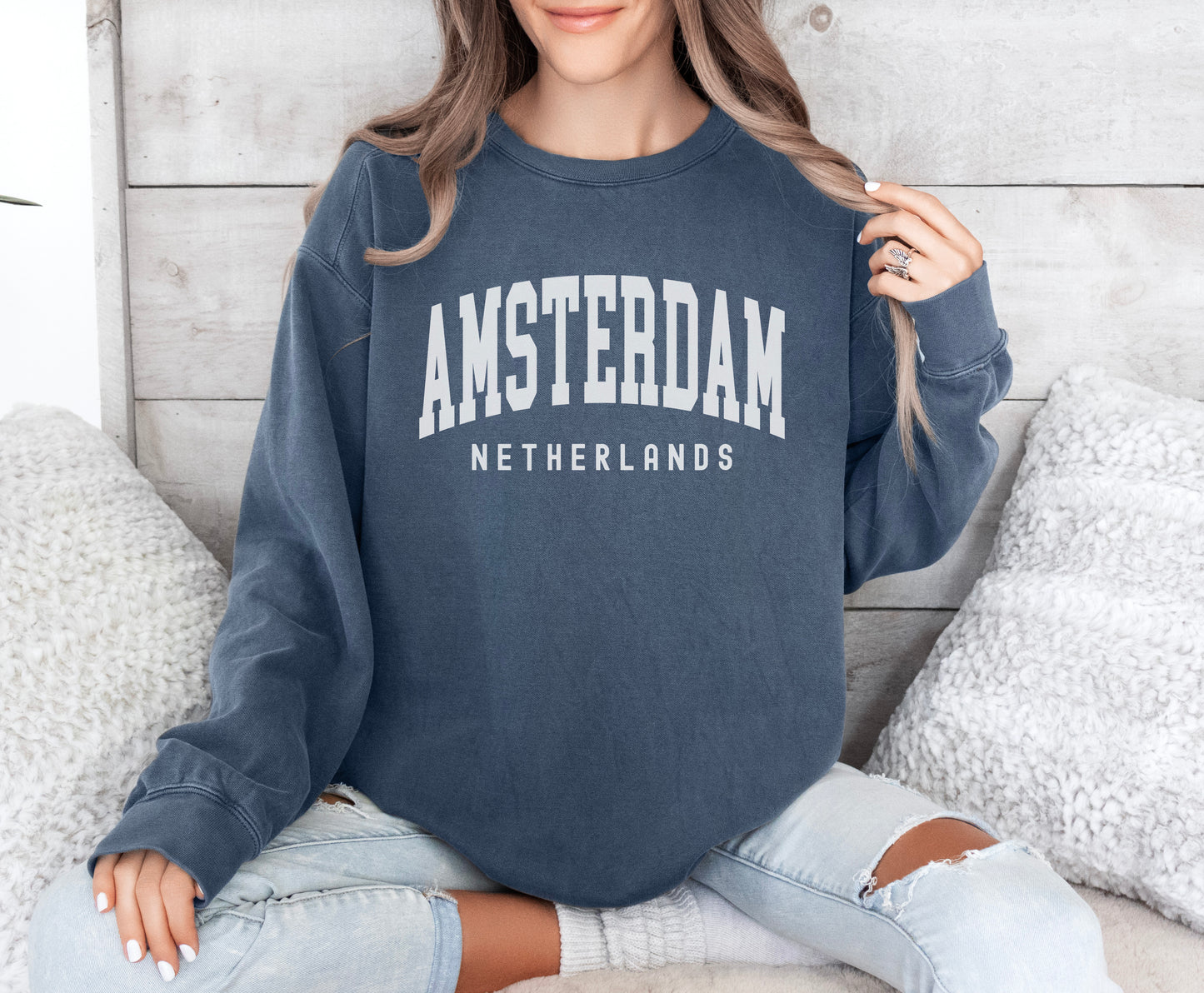 a woman sitting on a bed wearing an amsterdam sweatshirt