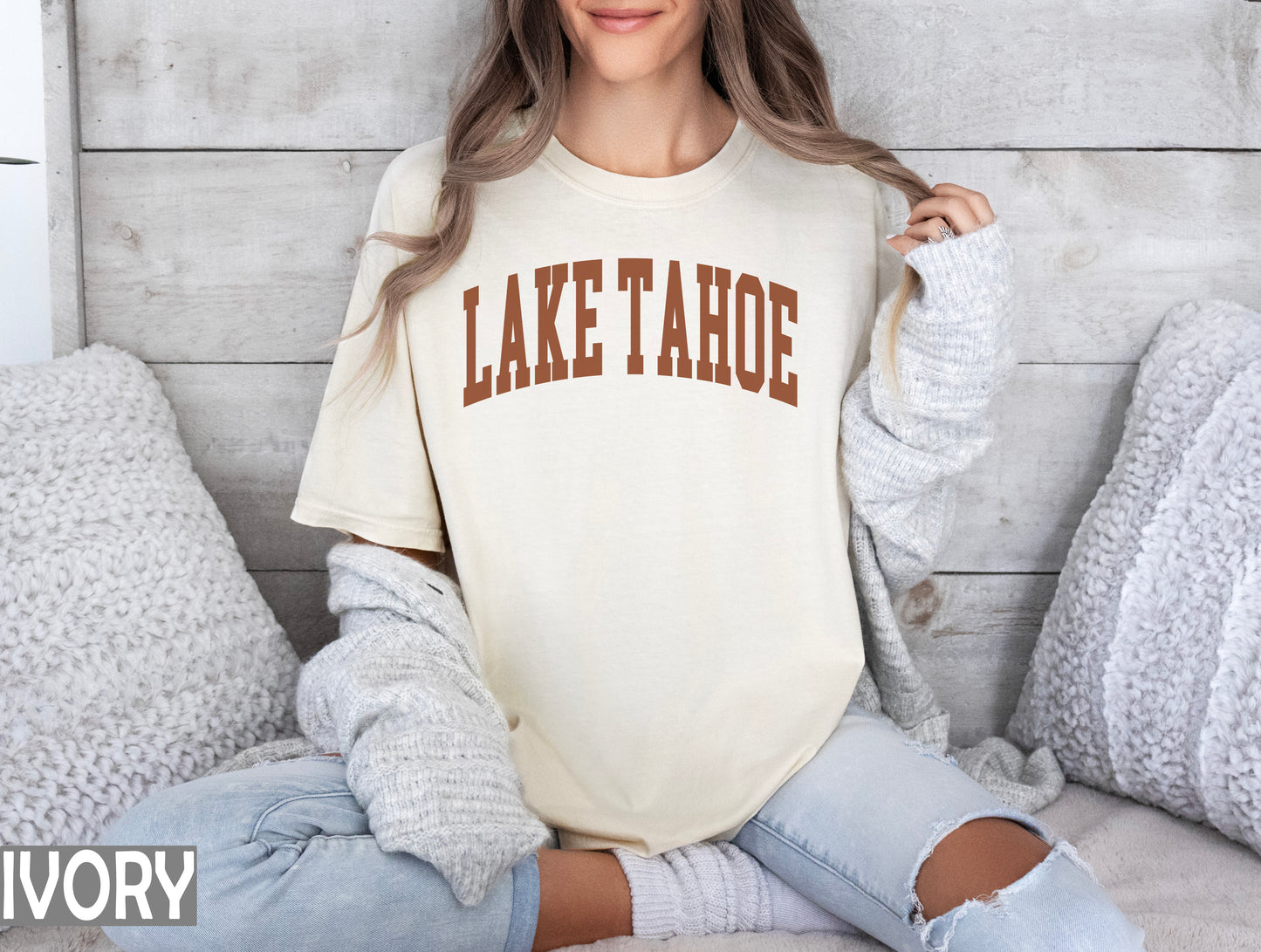 a woman sitting on a bed wearing a lake tahoe shirt