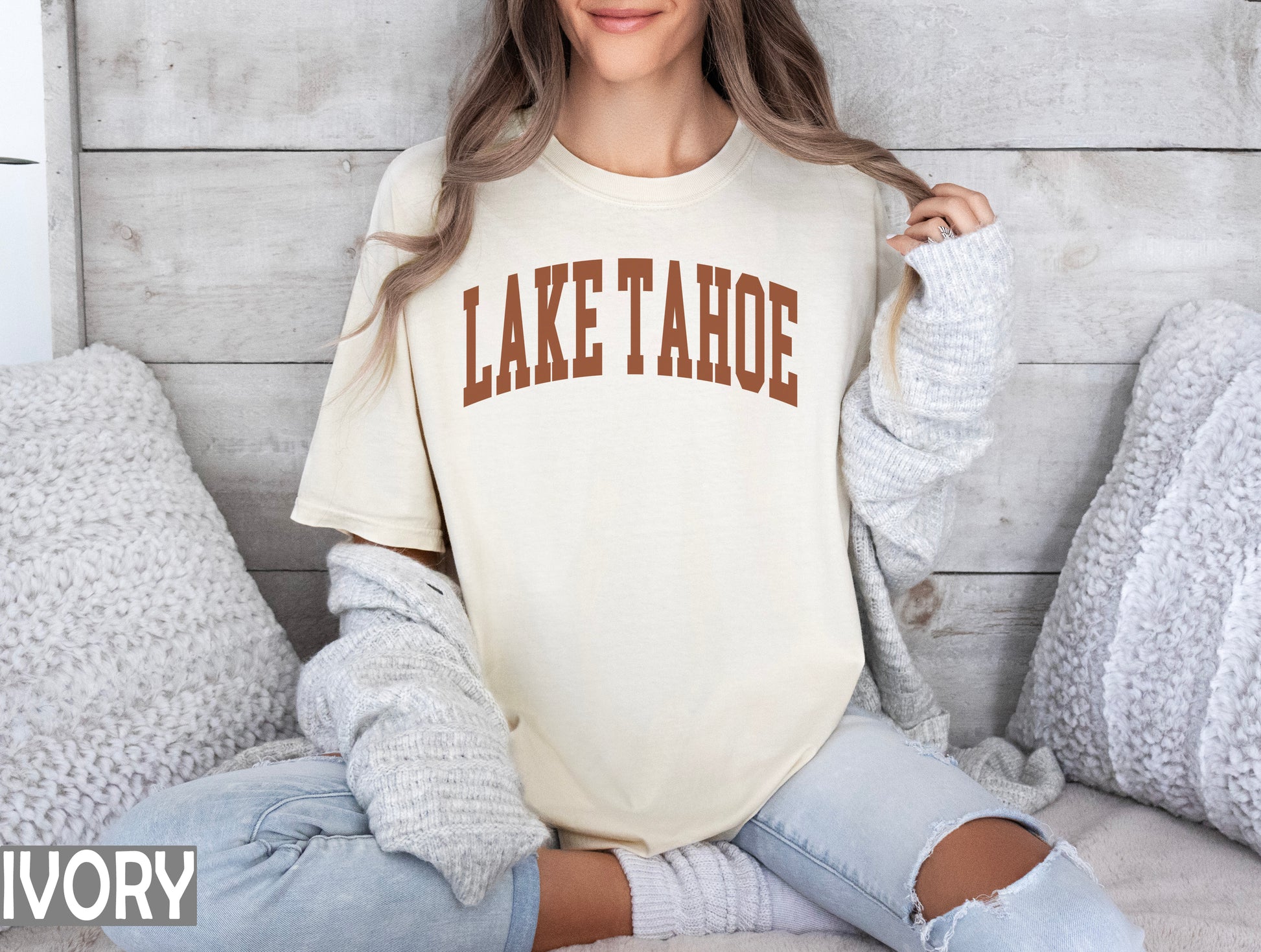 a woman sitting on a bed wearing a lake tahoe shirt