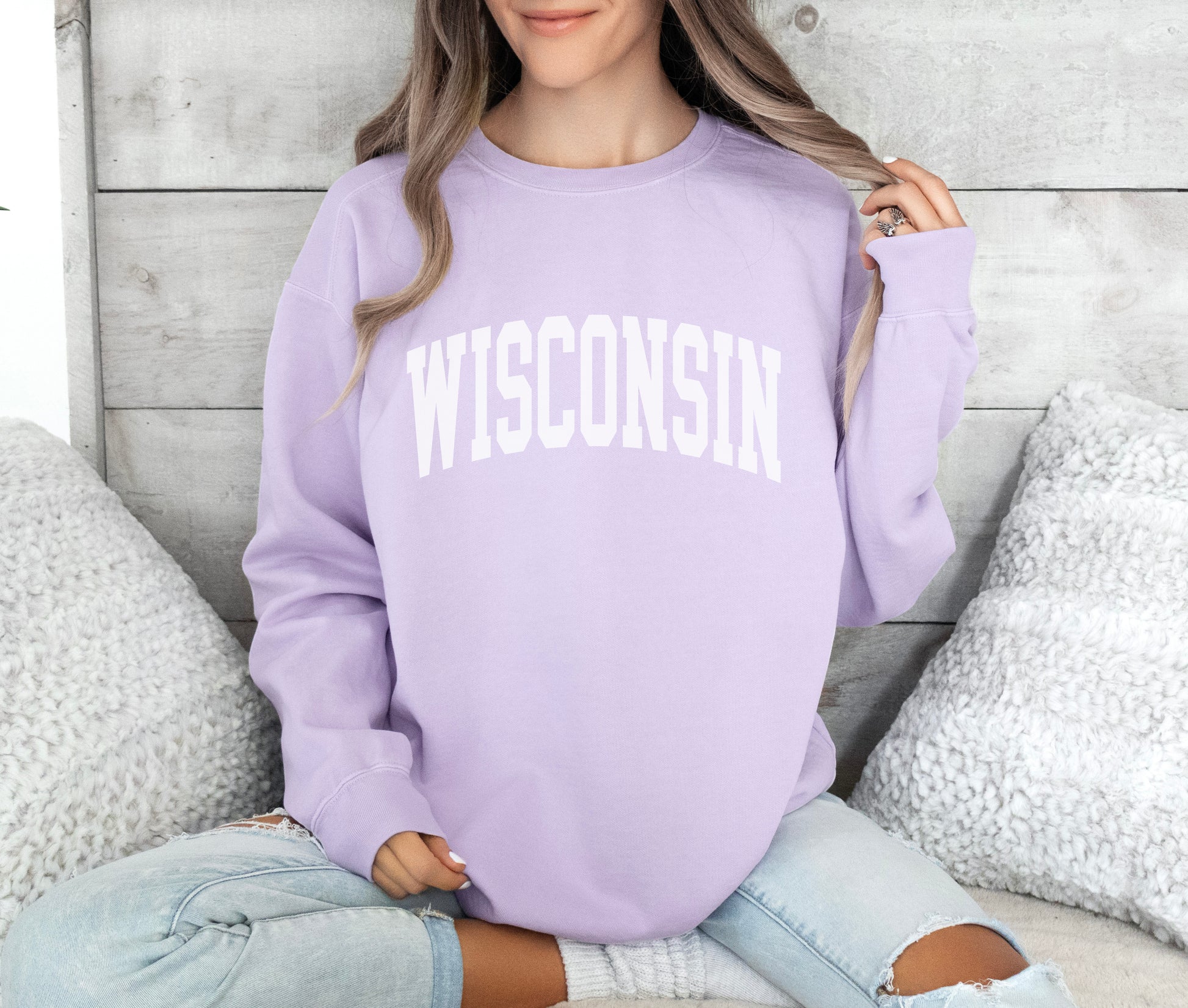 a woman sitting on a bed wearing a purple wisconsin sweatshirt