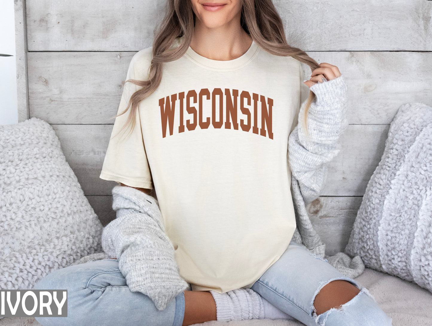 a woman sitting on a bed wearing a wisconsin t - shirt