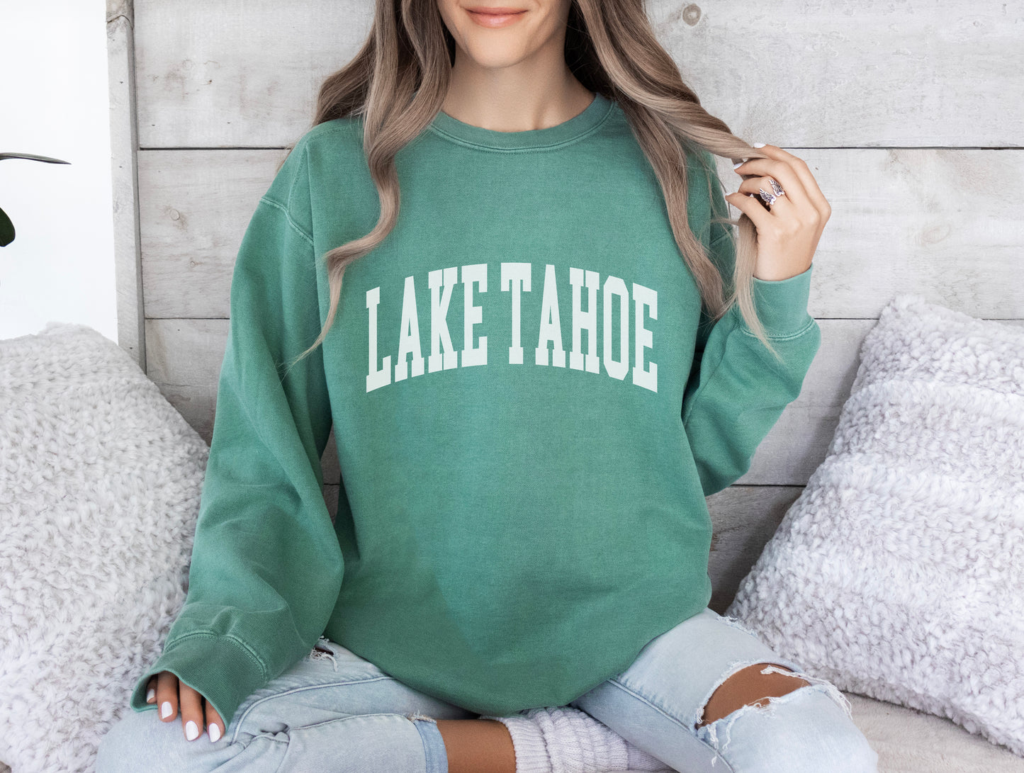 a woman sitting on a bed wearing a lake tahoe sweatshirt