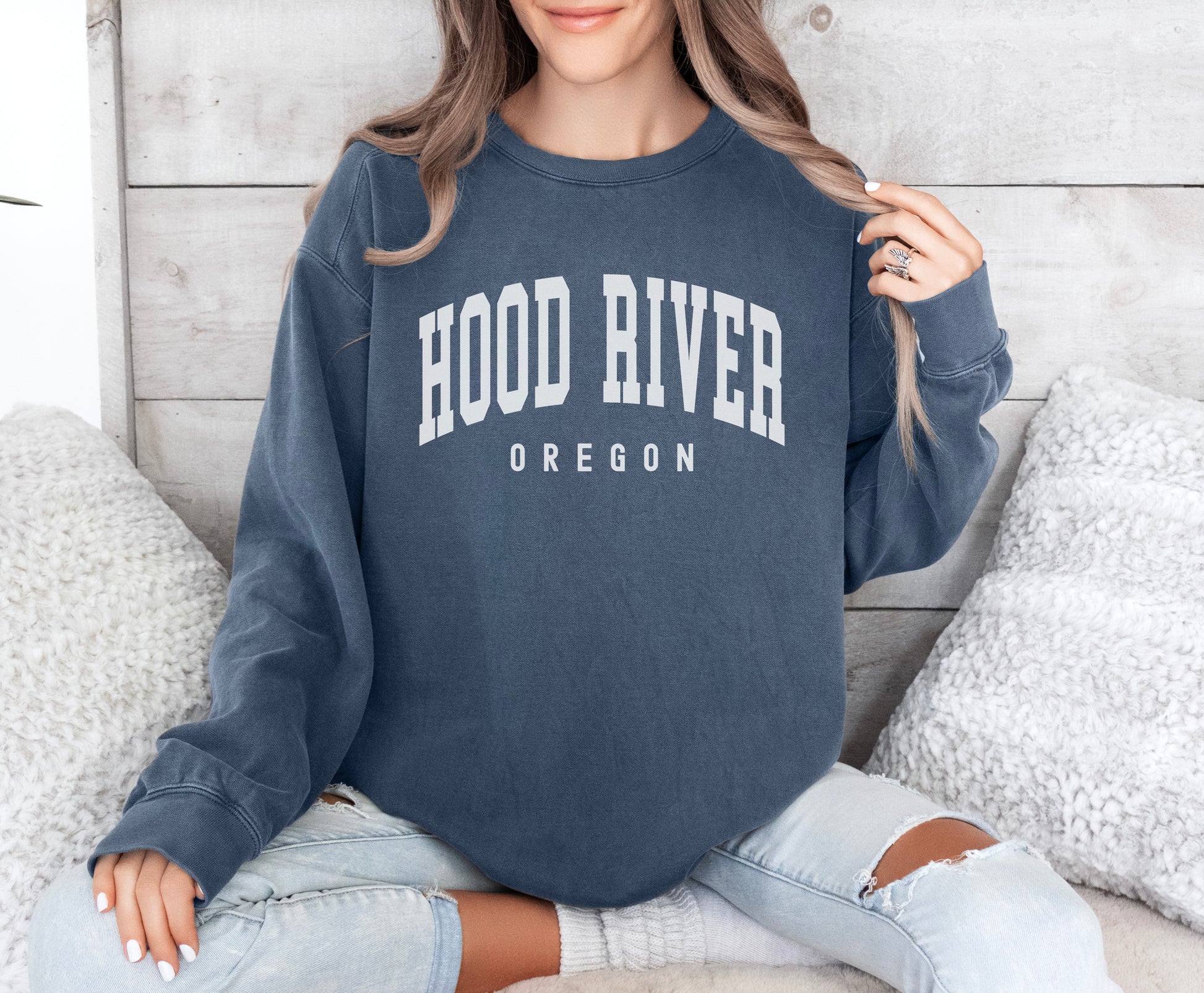 a woman sitting on a bed wearing a hood river oregon sweatshirt