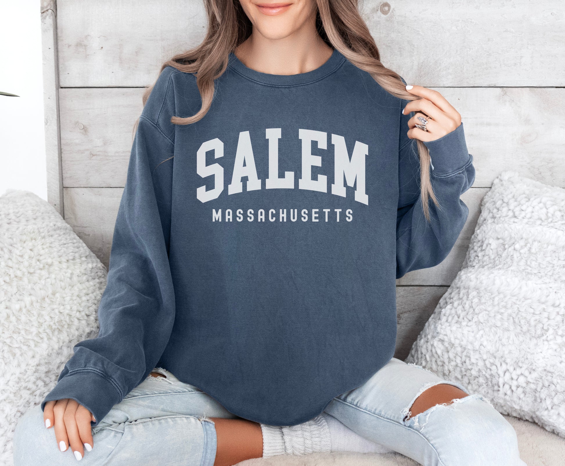 a woman sitting on a bed wearing a salem sweatshirt