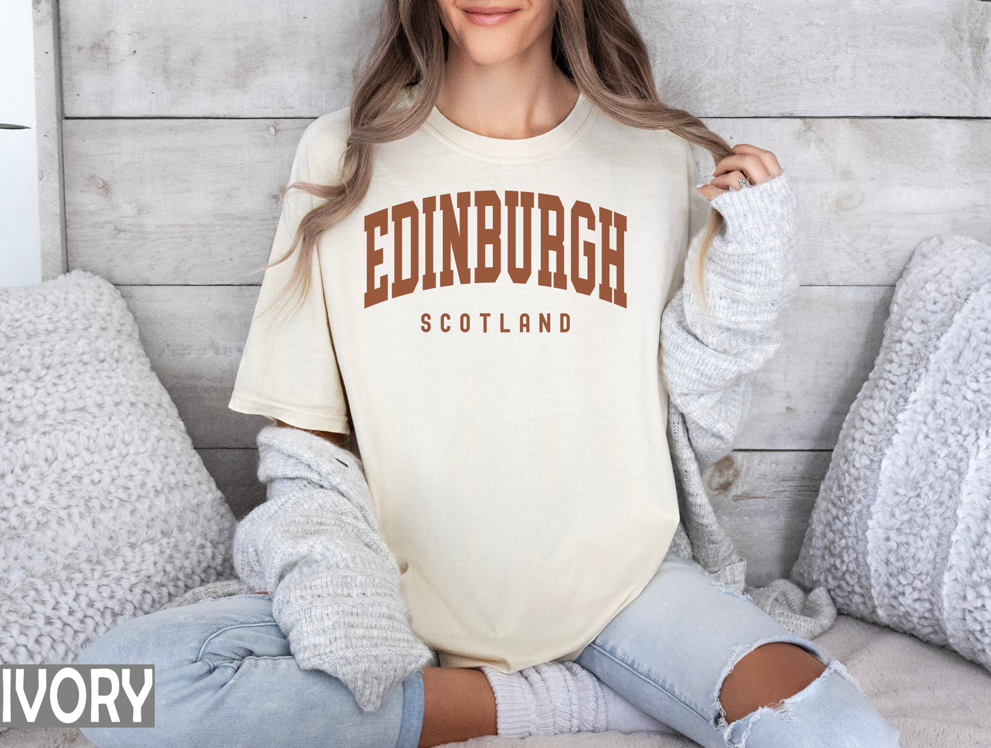 a woman sitting on a bed wearing a edinburgh t - shirt