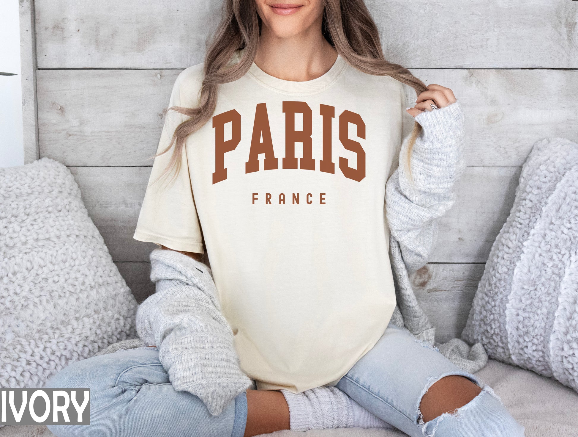 a woman sitting on a bed wearing a paris t - shirt