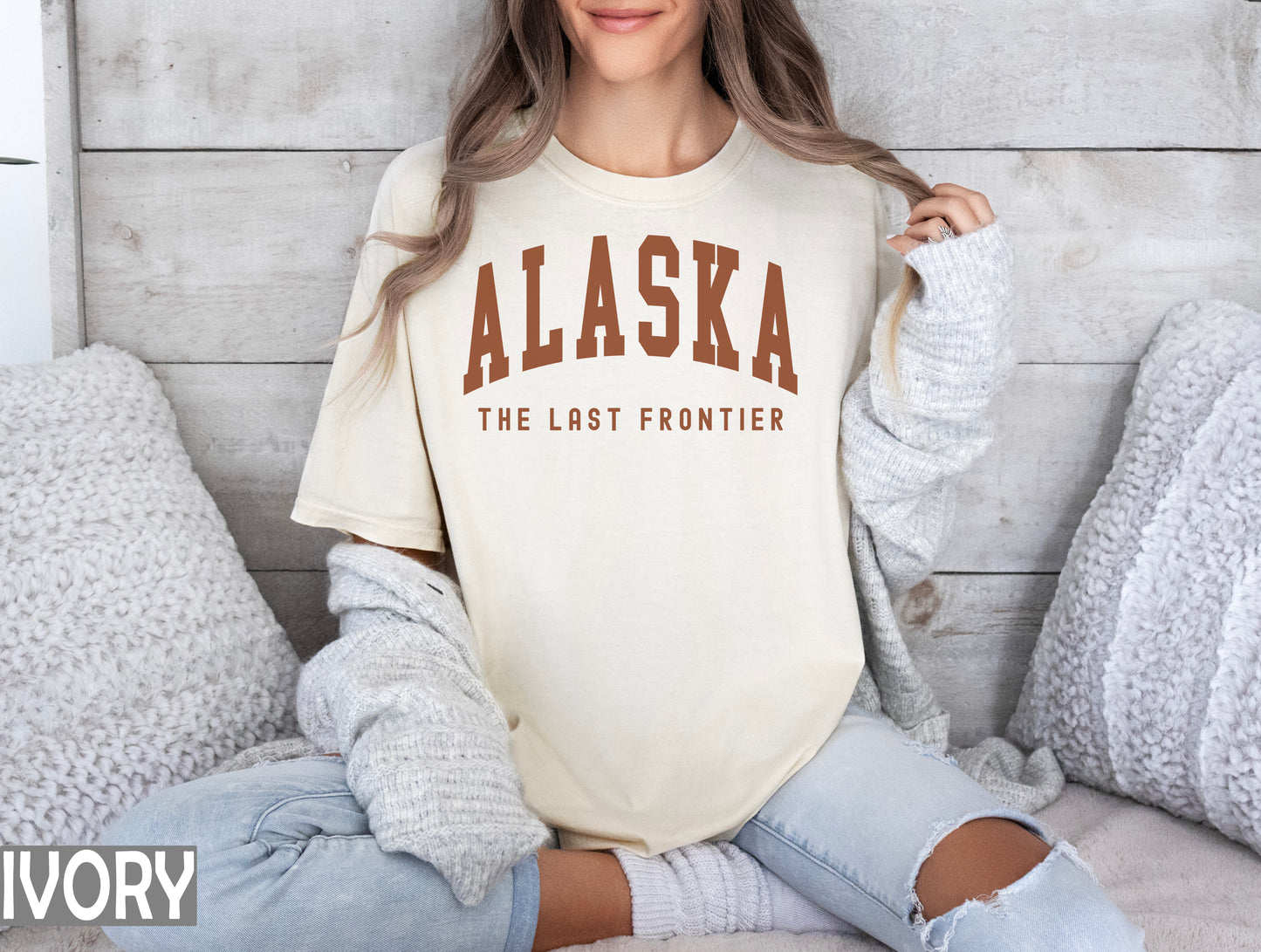 a woman sitting on a bed wearing a shirt that says alaska the last frontier