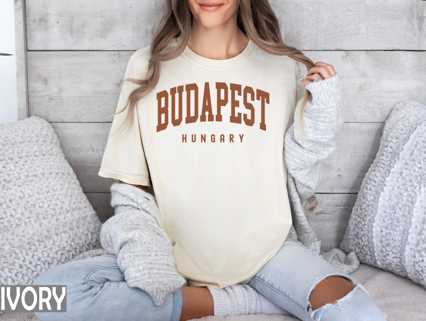 a woman sitting on a bed wearing a shirt that says buddapest