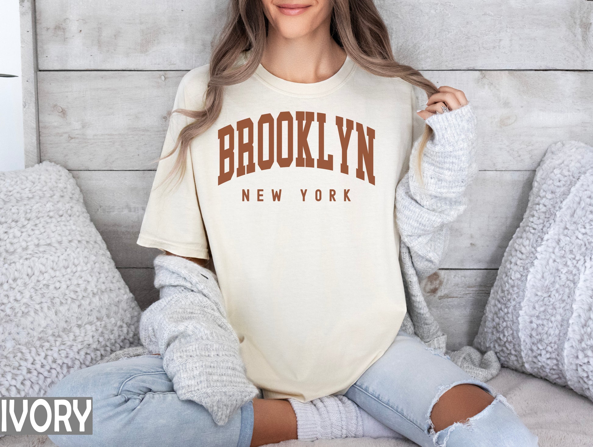 a woman sitting on a bed wearing a brooklyn t - shirt