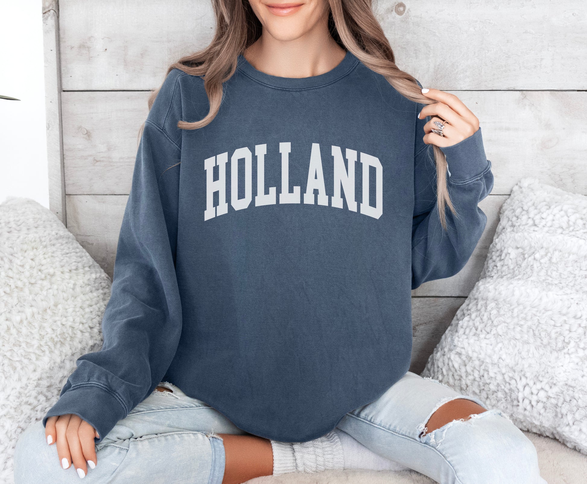 a woman sitting on a bed wearing a sweatshirt that says holland