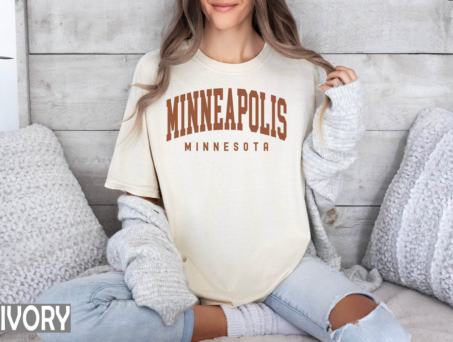 a woman sitting on a bed wearing a minnesota t - shirt