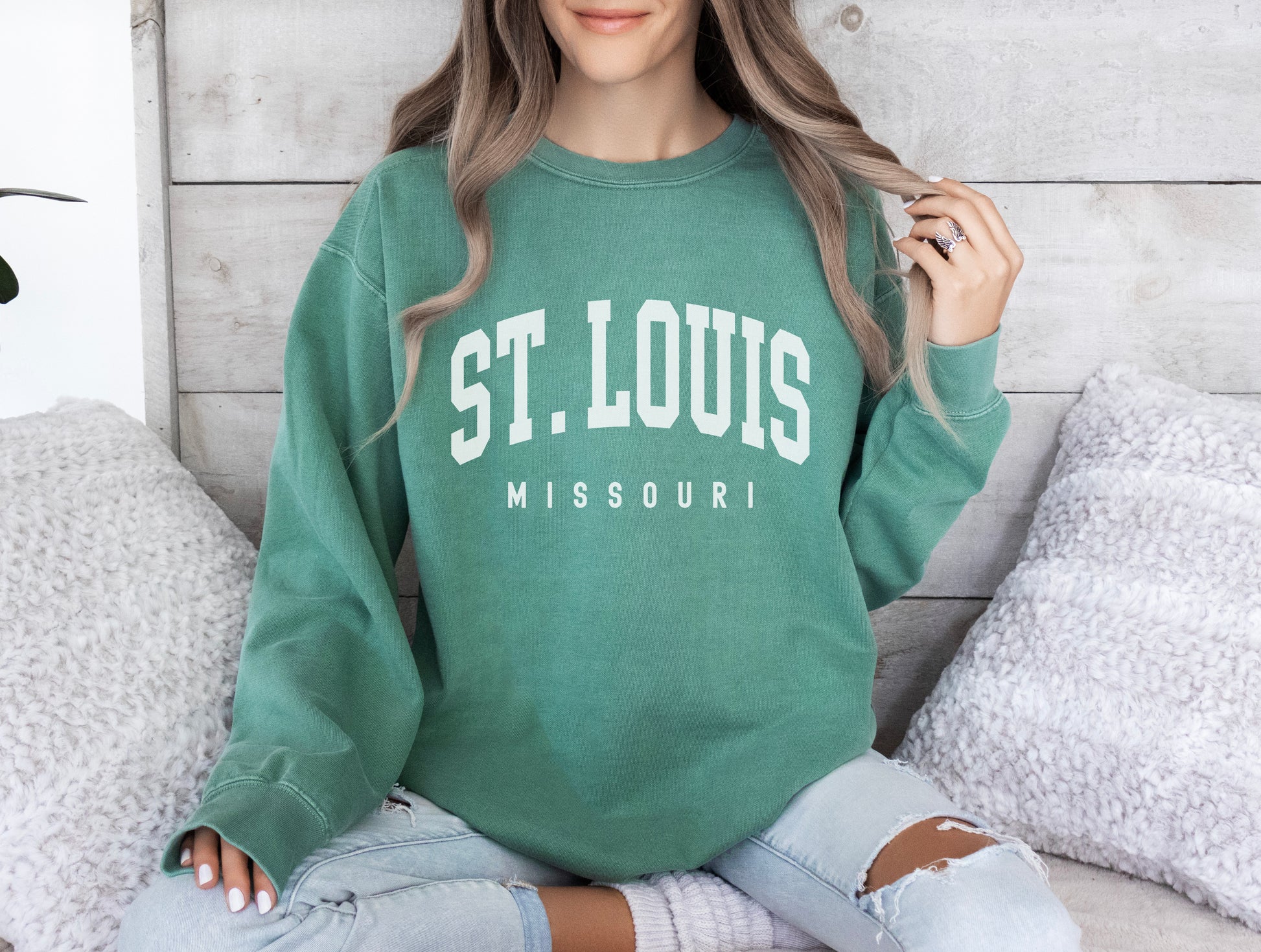 a woman sitting on a bed wearing a st louis sweatshirt