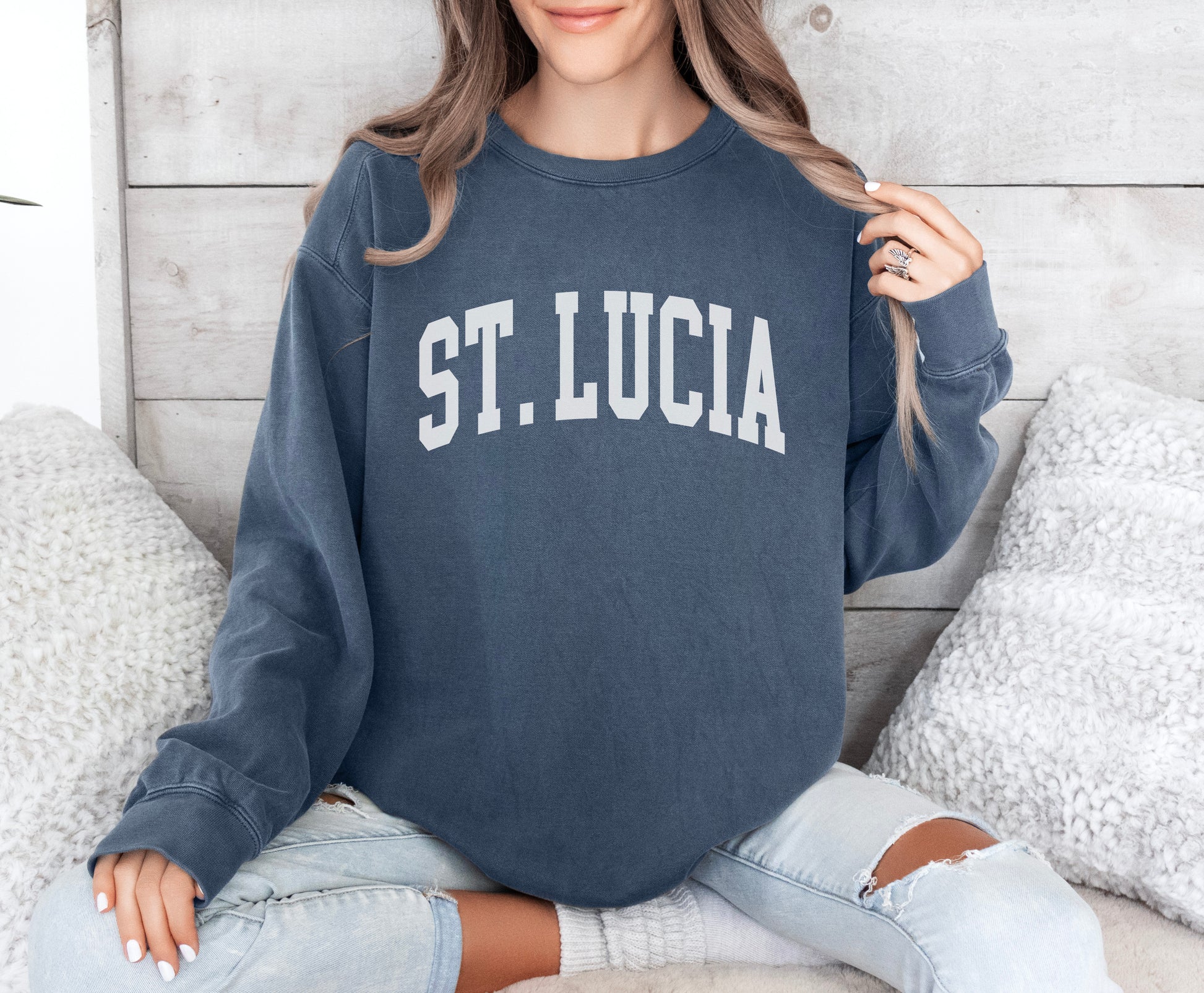 a woman sitting on a bed wearing a st lucia sweatshirt