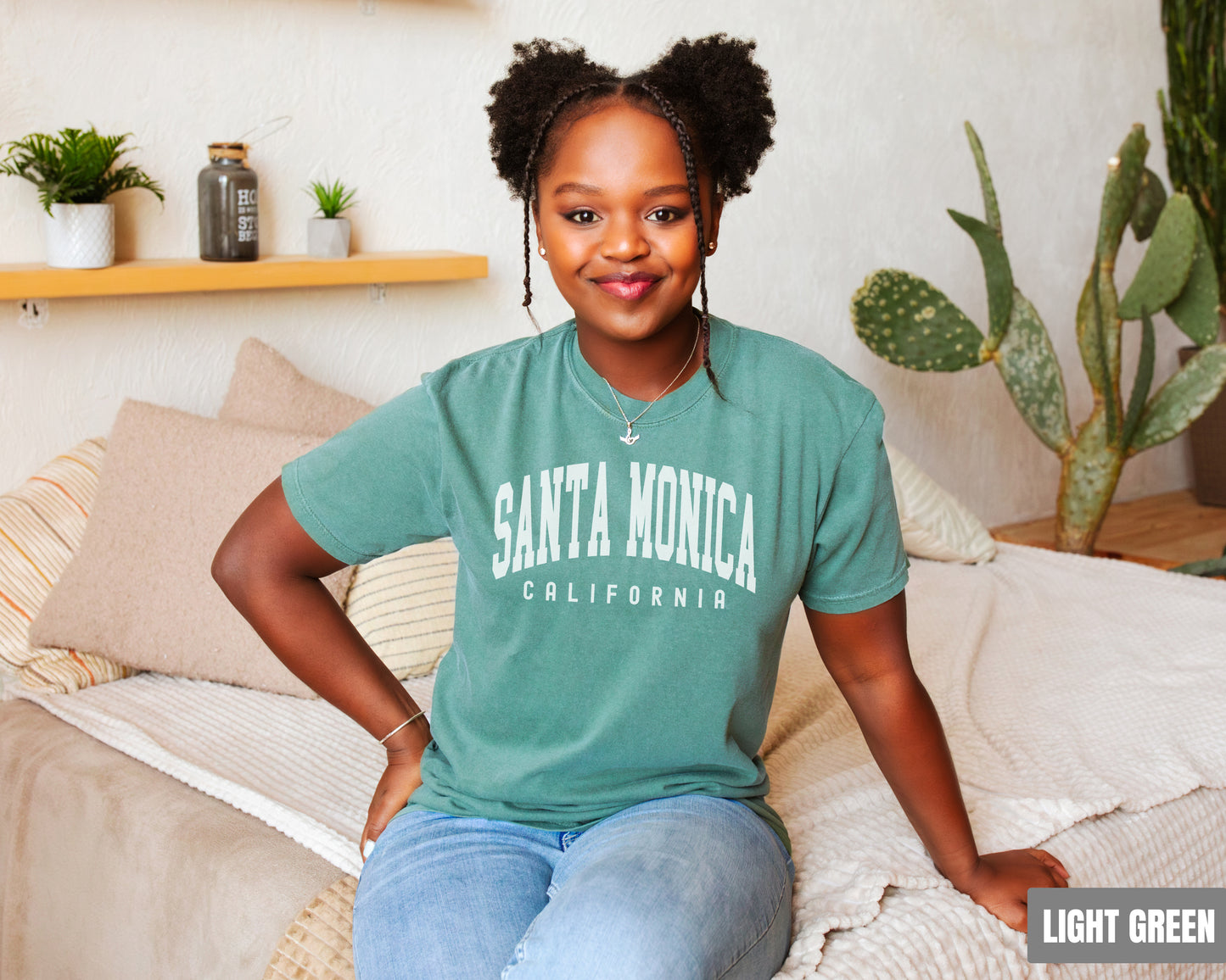 a woman sitting on top of a bed wearing a santa monica shirt