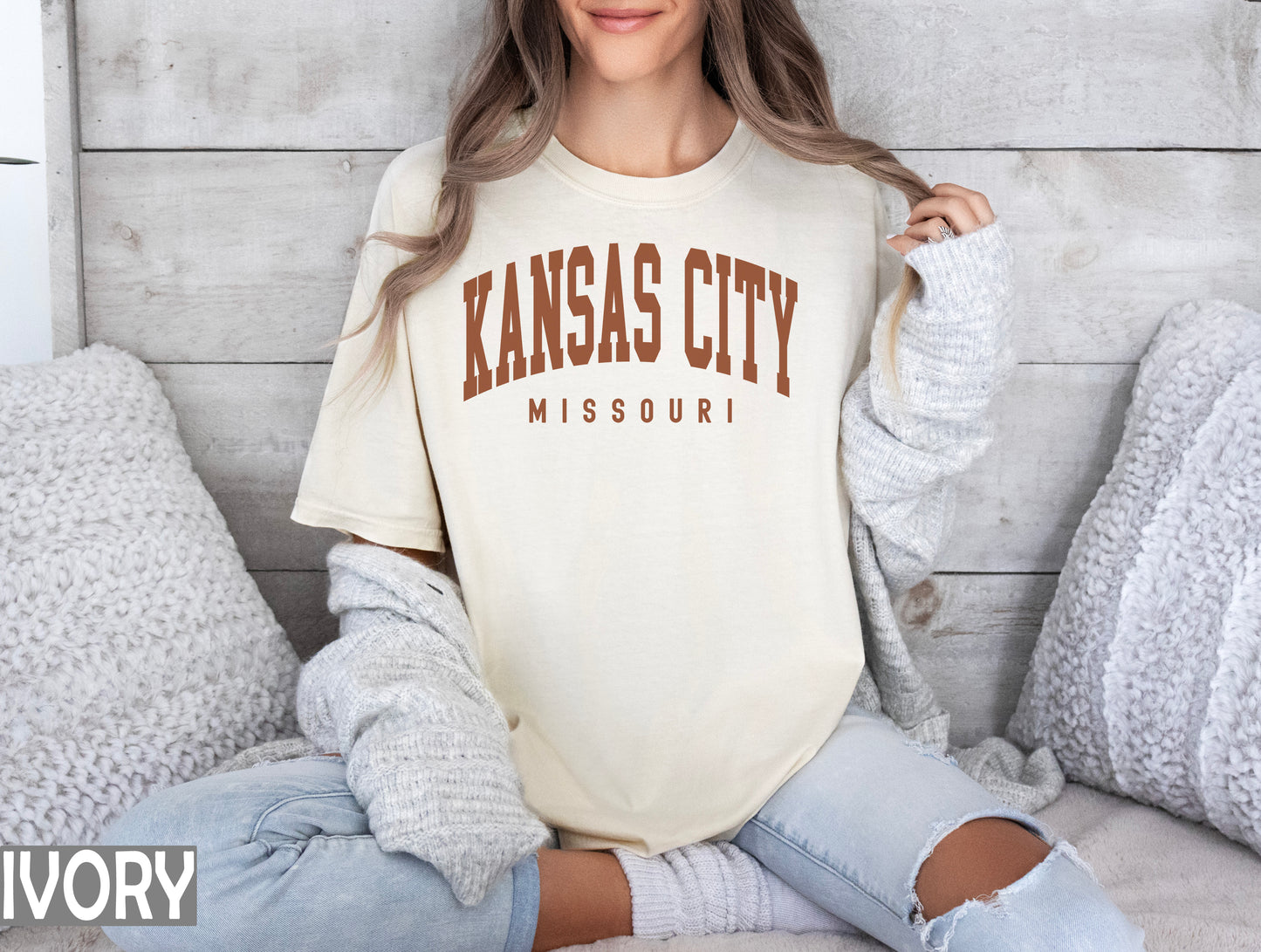 a woman sitting on a bed wearing a kansas city shirt