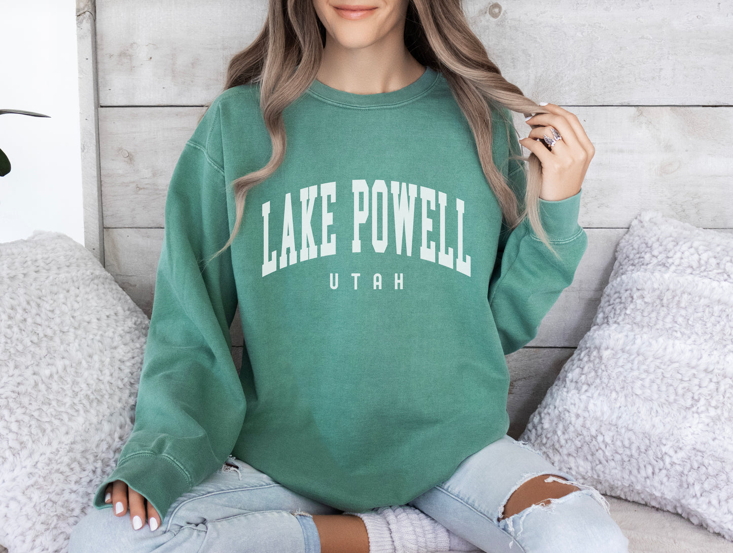 a woman sitting on a bed wearing a lake powell sweatshirt