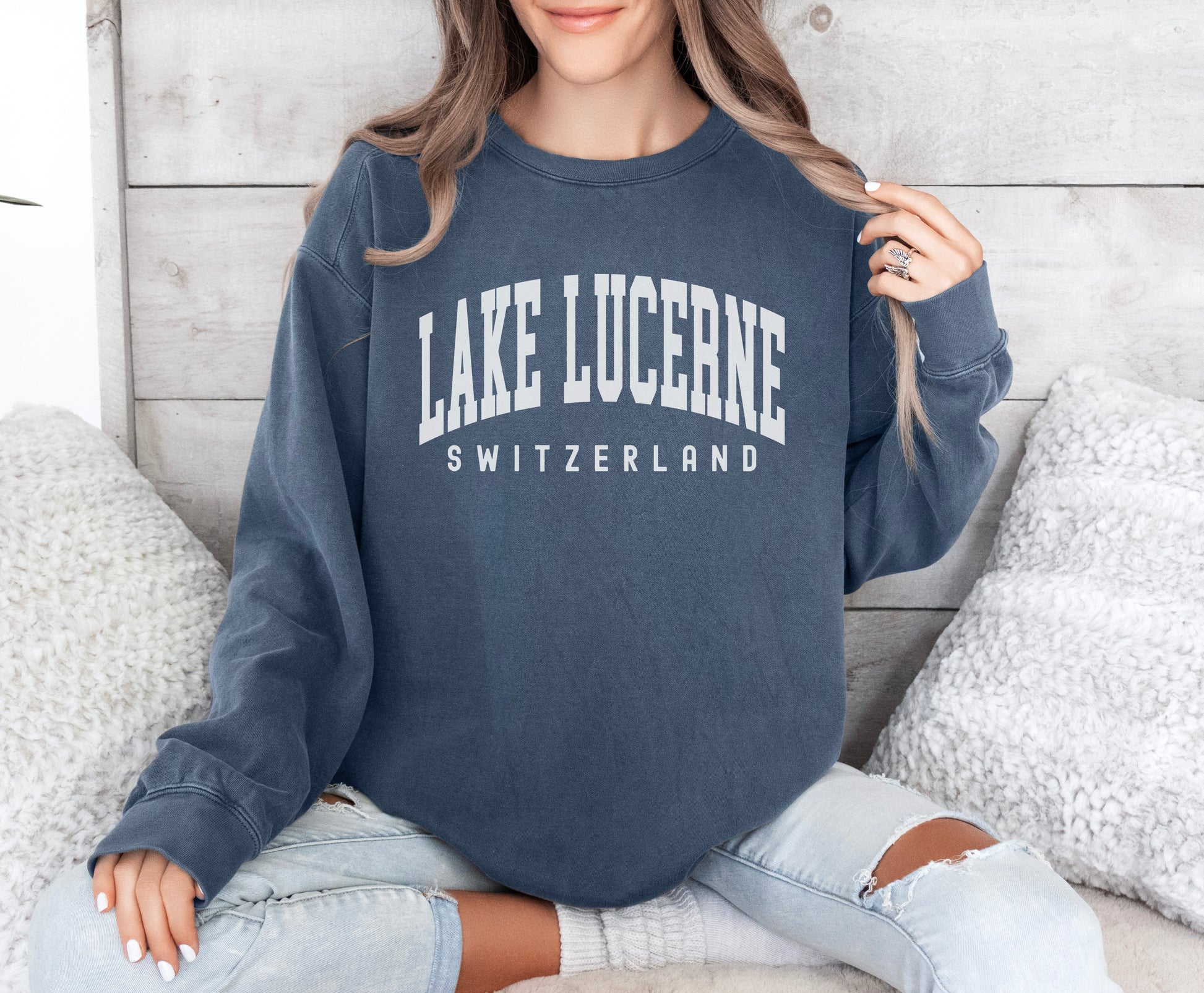 a woman sitting on a bed wearing a lake luceine sweatshirt