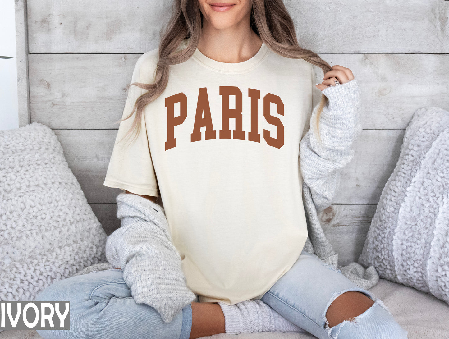 a woman sitting on a bed wearing a shirt that says paris