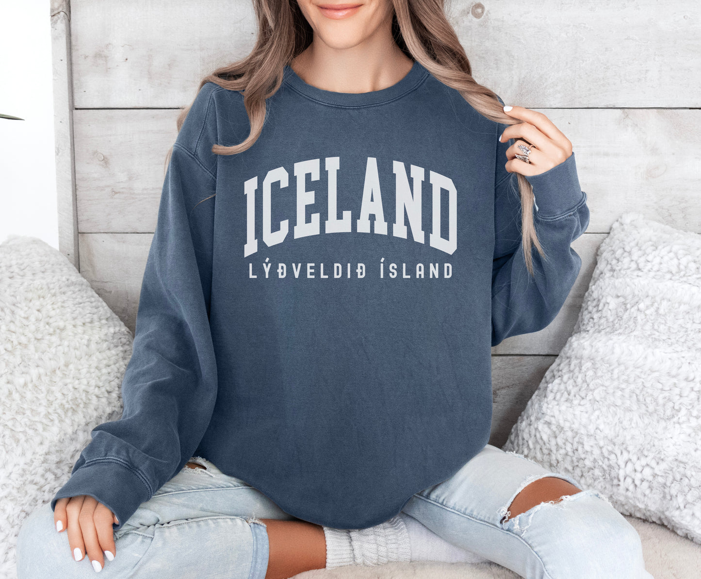 a woman sitting on a bed wearing a iceland sweatshirt