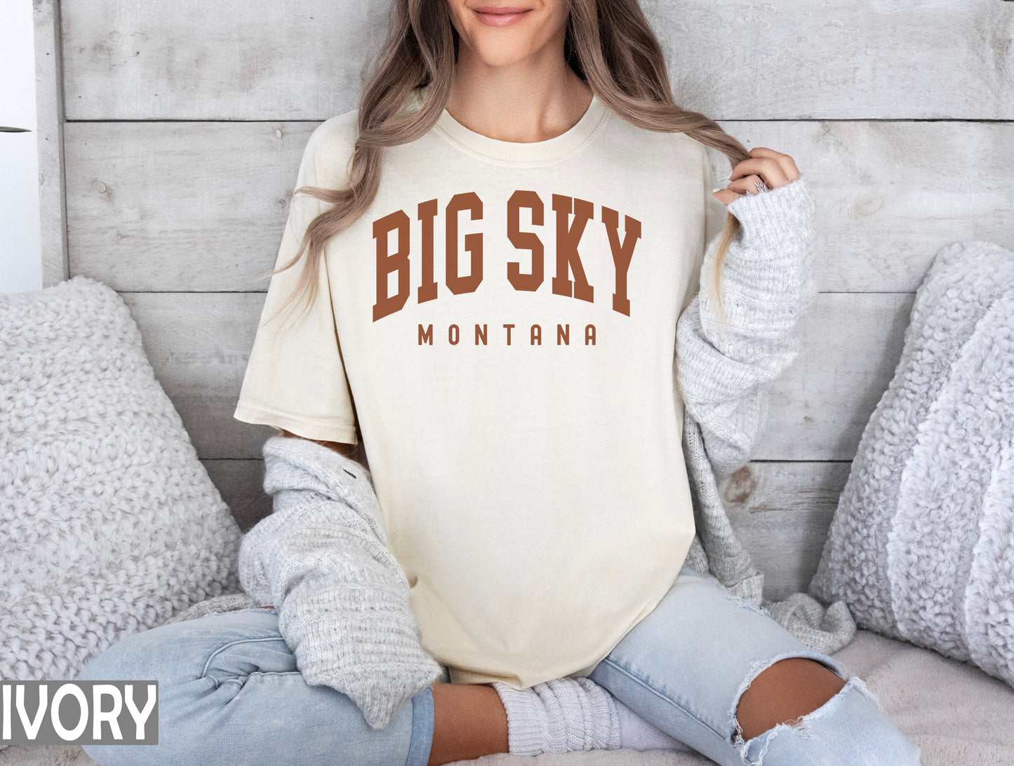 a woman sitting on a bed wearing a big sky shirt