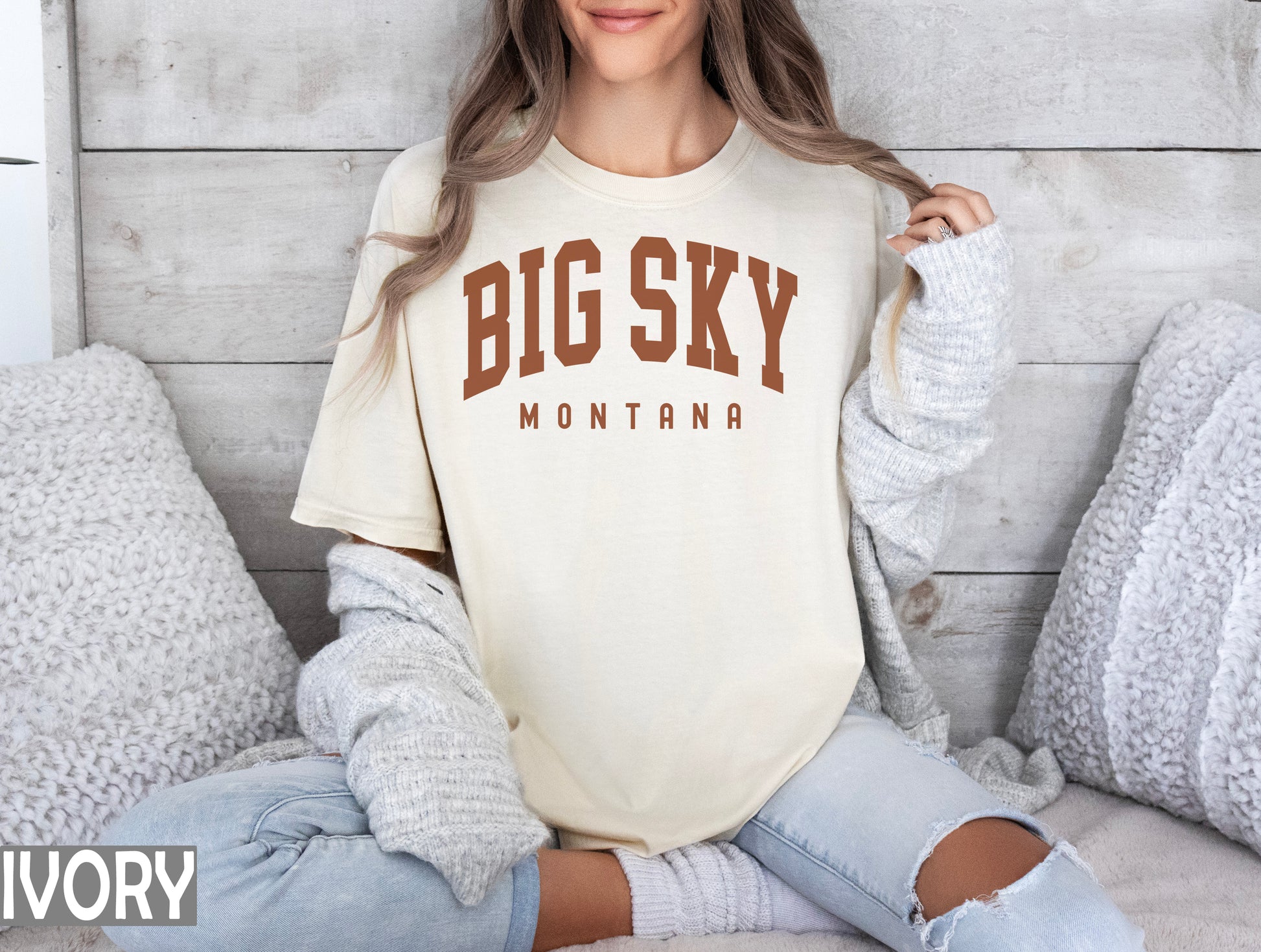 a woman sitting on a bed wearing a big sky shirt