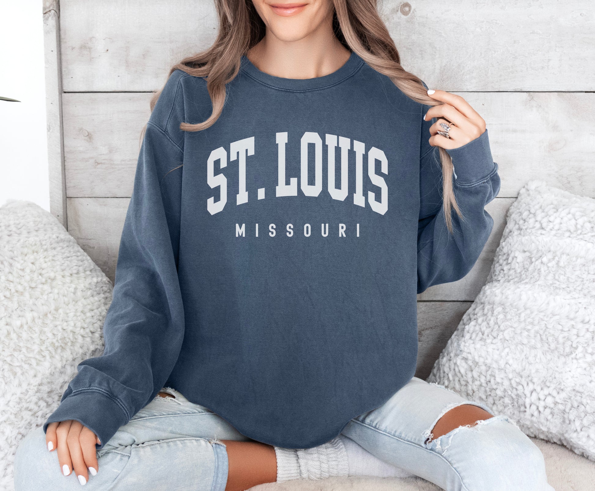 a woman sitting on a bed wearing a st louis sweatshirt