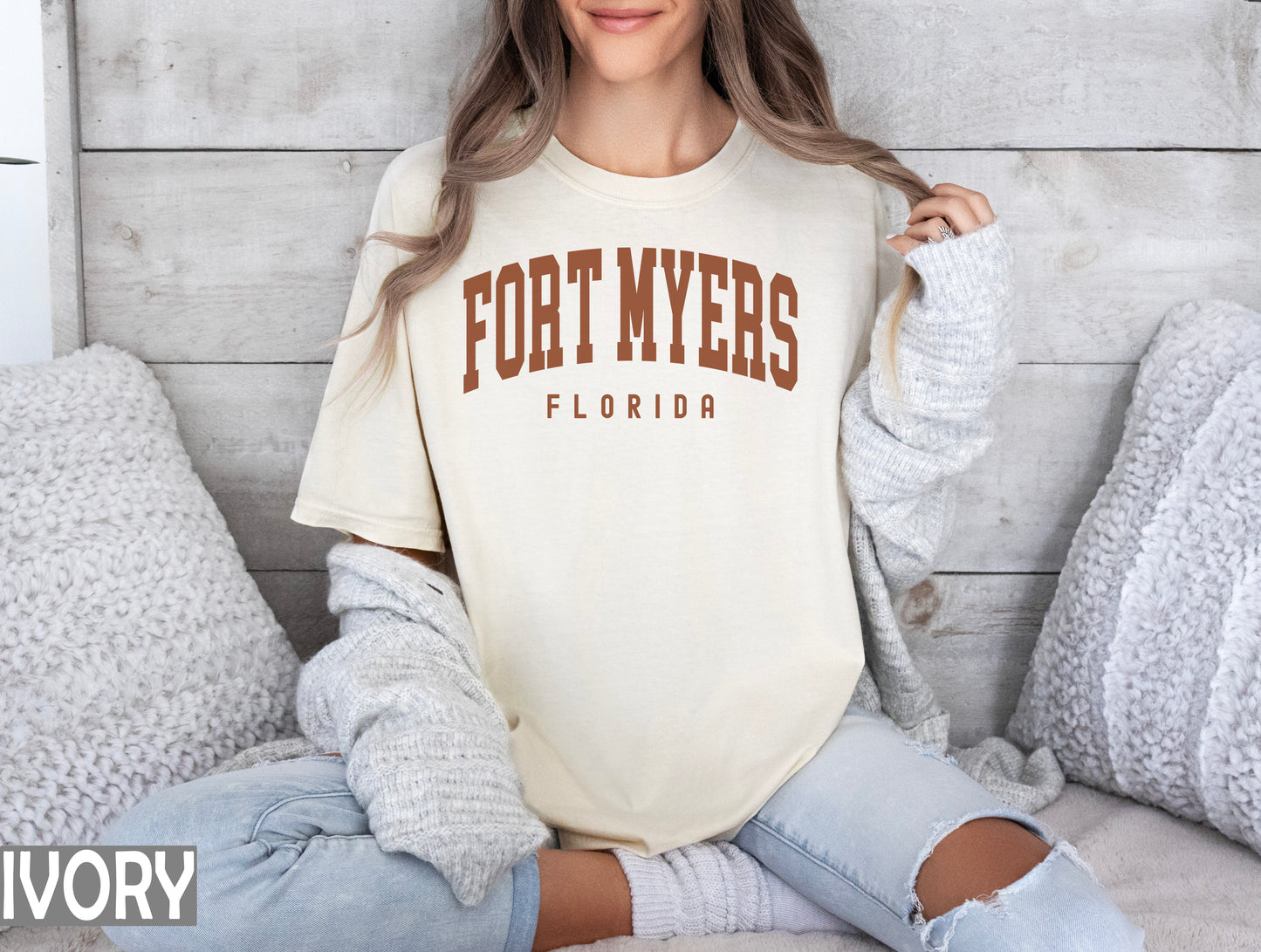 a woman sitting on a bed wearing a fort myers shirt