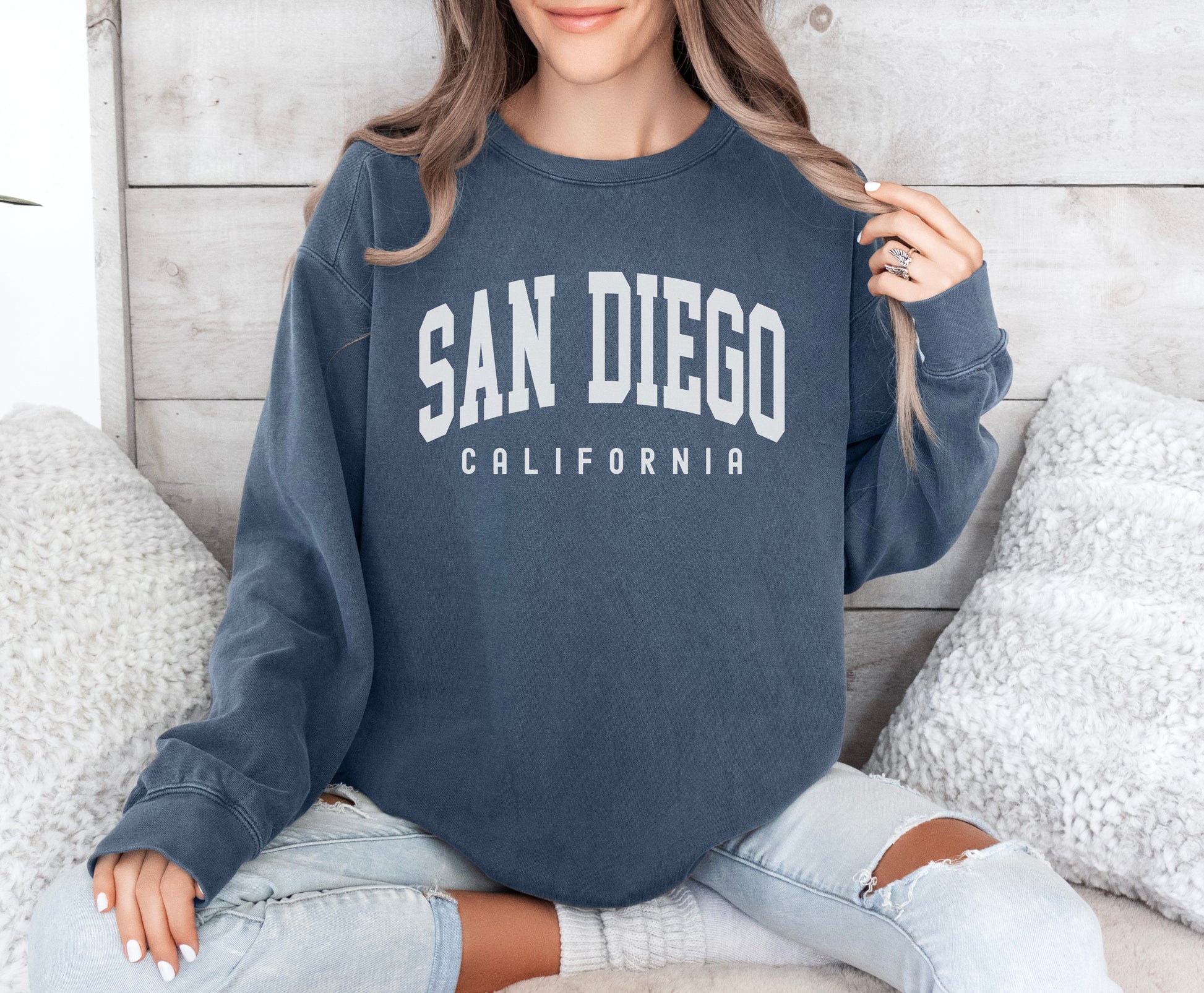 a woman sitting on a bed wearing a san diego sweatshirt