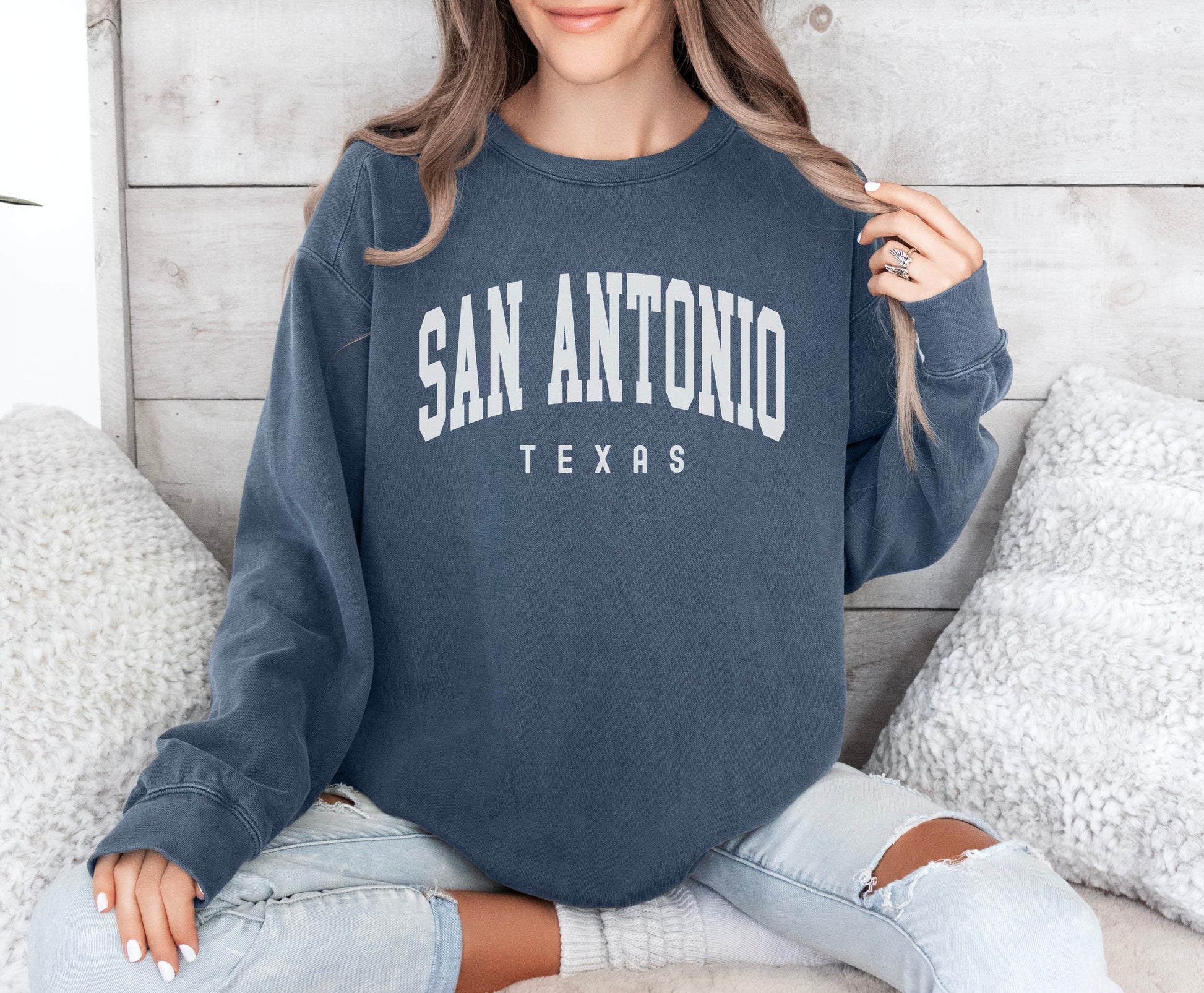 a woman sitting on a bed wearing a san antonio sweatshirt