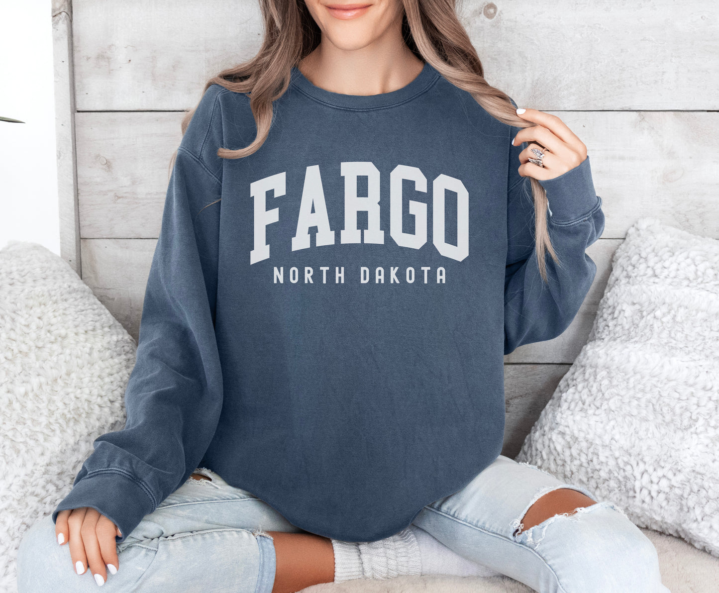 a woman sitting on a bed wearing a sweatshirt that says fargo