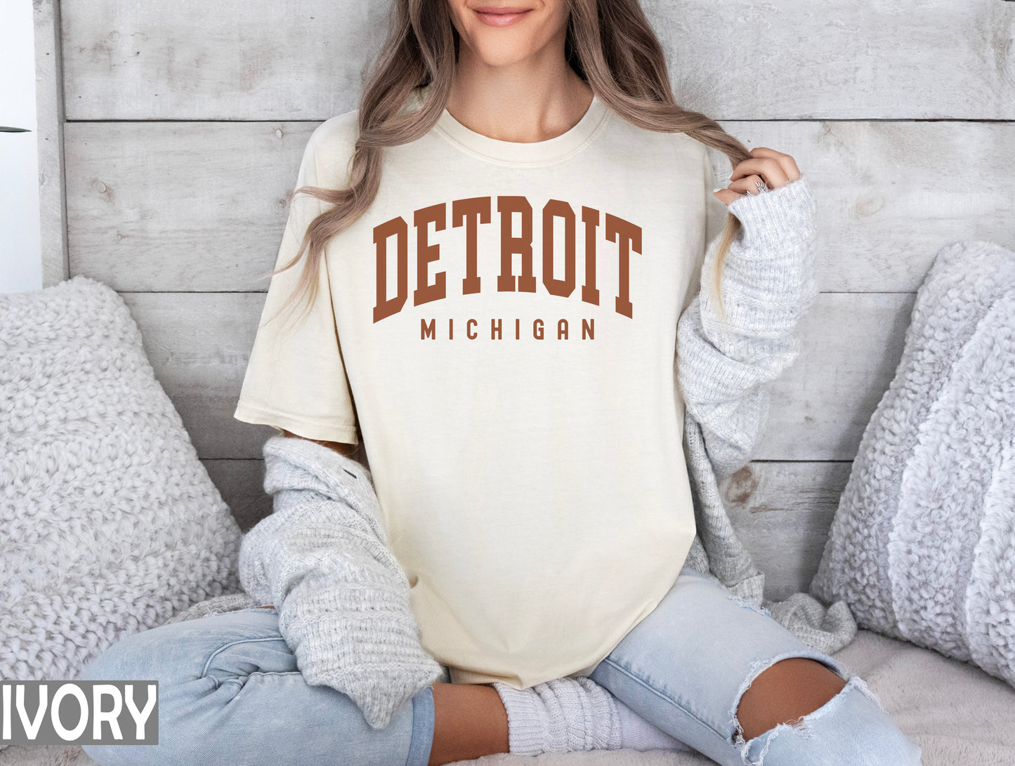 a woman sitting on a bed wearing a detroit michigan t - shirt