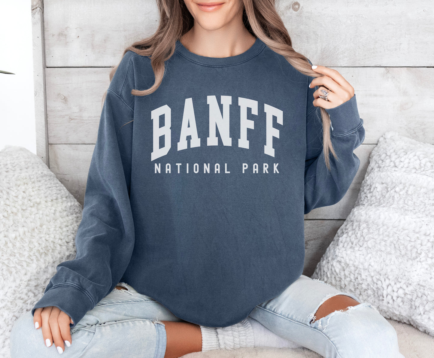 a woman sitting on a bed wearing a sweatshirt that says banff national park