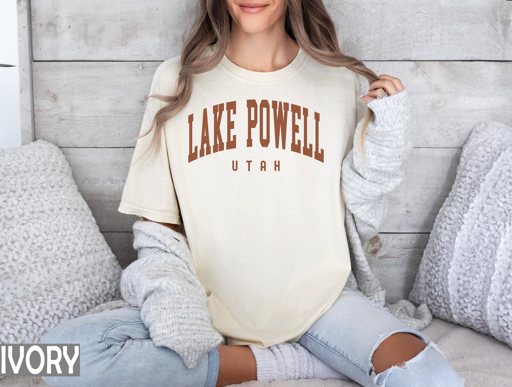 a woman sitting on a bed wearing a lake powell shirt